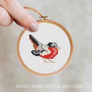 May include: A cross stitch pattern of a small red robin bird with a black head and brown wings. The pattern is in a wooden embroidery hoop.