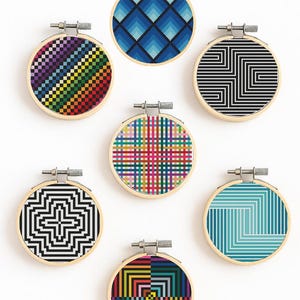 May include: Seven embroidery hoops with geometric patterns. Designs include a rainbow gradient, blue diamonds, black and white lines, a colourful plaid, and a teal and white design. Each hoop is set in a wooden frame.