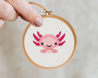 May include: A pink and white cross-stitch embroidery of an axolotl in a wooden embroidery hoop.