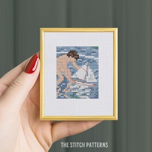 May include: A cross-stitch pattern of a person in the water with a sailboat. The person is nude and has brown hair. The water is blue and green. The sailboat is white with a red sail.