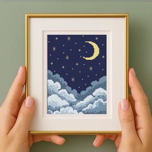 Pode incluir: Uma obra de arte em ponto cruz emoldurada que retrata uma cena noturna. O design apresenta uma lua crescente, estrelas e nuvens fofas em tons de azul e branco. A obra de arte está emoldurada em uma moldura dourada.