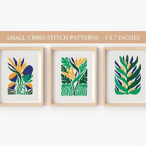 May include: Three framed cross stitch patterns featuring stylized floral designs in shades of green, blue, and yellow. Each pattern is 5 inches by 7 inches.