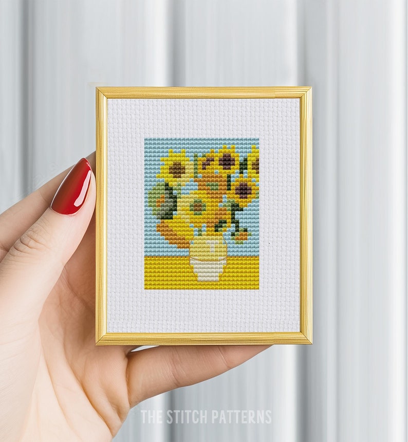 May include: A cross-stitch pattern of a vase of sunflowers in a yellow, blue, and green color scheme. The pattern is framed in a gold frame.