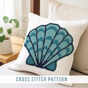 May include: White square pillow with a cross-stitch design of a teal seashell. The seashell design has a dark blue outline and is filled with shades of teal. The text "CROSS STITCH PATTERN" is at the bottom.