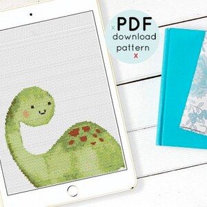 May include: A digital tablet displaying a cross-stitch pattern of a green dinosaur with red spots. The text "PDF download pattern" is displayed on the screen.