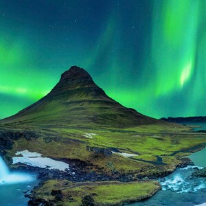 May include: A green aurora borealis, also known as the Northern Lights, illuminates the night sky above a mountain and a waterfall.