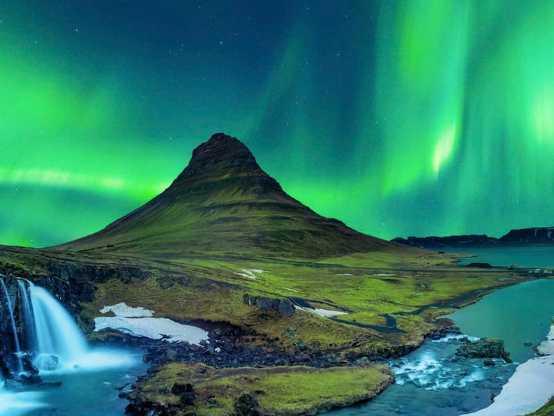 May include: A green aurora borealis, also known as the Northern Lights, illuminates the night sky above a mountain and a waterfall.