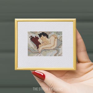 May include: A cross-stitch pattern of a couple embracing in a bed, with a red blanket and a gold bracelet on the woman's wrist.