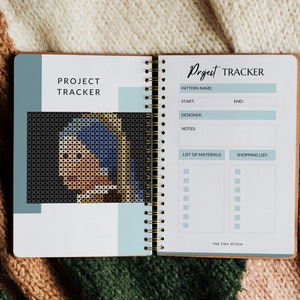 Pode incluir: Um caderno de rastreamento de projetos com uma capa azul e branca. O caderno tem uma encaderna&ccedil;&atilde;o em espiral e uma se&ccedil;&atilde;o para listar os materiais e uma lista de compras. A capa apresenta uma imagem pixelada de uma mulher com um len&ccedil;o azul.