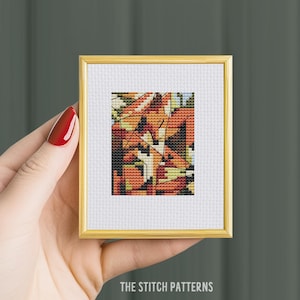 May include: A framed cross-stitch pattern with a geometric design featuring abstract shapes in shades of orange, yellow, and white.