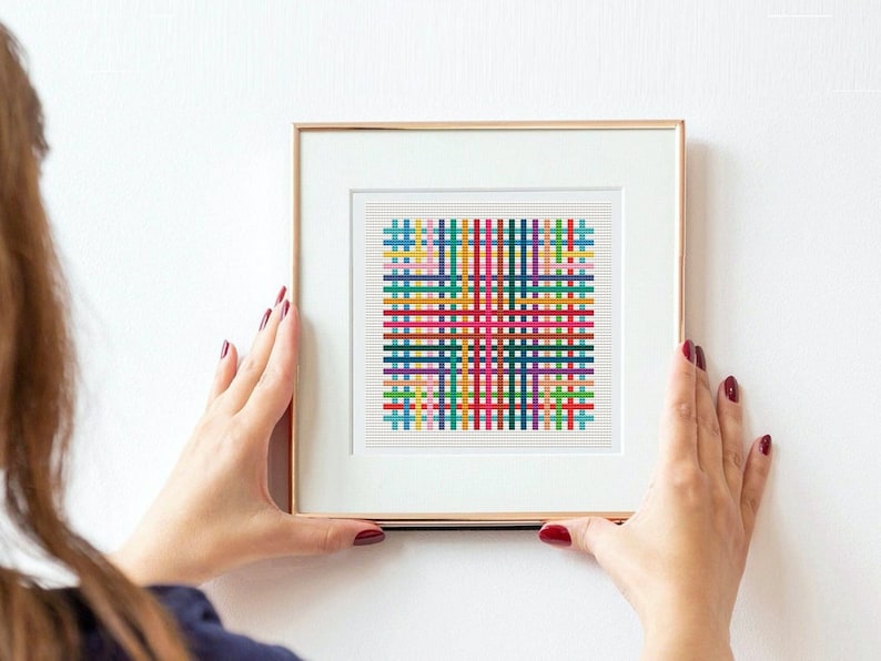Op de afbeelding: Een ingelijst abstract kunstprint met een kleurrijk geometrisch patroon van elkaar kruisende lijnen in tinten rood, blauw, groen, geel en roze.