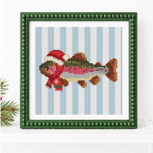 May include: A cross-stitch embroidery of a fish wearing a red and white Santa hat and a red scarf with a white snowflake pattern. The fish is positioned against a background of vertical light blue and white stripes, encased in a dark green frame.