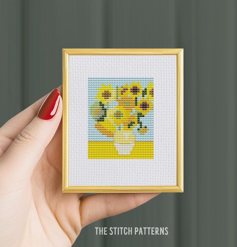 May include: A framed cross-stitch pattern of a vase of sunflowers. The sunflowers are yellow and the vase is white. The background is blue and yellow.