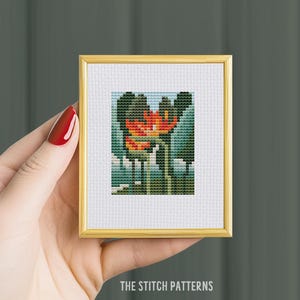 Puede incluir: Un patrón de punto de cruz de una flor roja con hojas verdes, enmarcado en un marco dorado.
