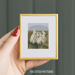 May include: A framed cross-stitch pattern featuring three white rabbits standing in a field with a blue sky above. The rabbits are facing each other and have their ears up. The field is green and the sky is a light blue with a few clouds. The frame is gold.