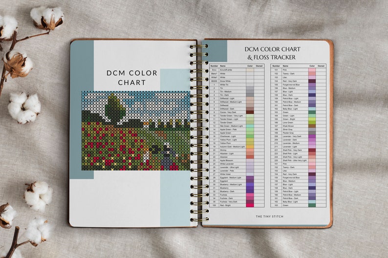 Pode incluir: Caderno aberto em espiral com uma tabela de cores e um rastreador de linha para ponto cruz. A tabela tem n&uacute;meros e nomes de cores DMC com as cores de linha correspondentes. A capa apresenta um padr&atilde;o de ponto cruz de um campo de flores vermelhas.