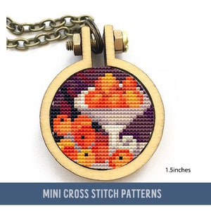 May include: A small wooden hoop with a cross stitch design of orange and purple fruit in a bowl. The hoop is 1.5 inches in diameter and is attached to a chain necklace. "MINI CROSS STITCH PATTERNS" is printed below the hoop.