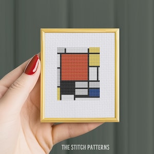 以下が含まれることがあります： 赤、黄、青、黒、グレーの正方形で構成された幾何学的な抽象的なデザインの額装されたクロスステッチパターンです。