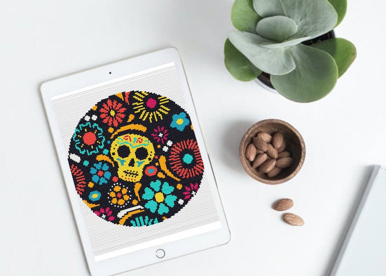K&ouml;nnte beinhalten: Eine digitale Illustration eines bunten Zucker-Sch&auml;dels, umgeben von Blumen auf schwarzem Hintergrund. Der Sch&auml;del ist gelb mit schwarzen Augen und einer rosa Zunge. Die Blumen sind rot, orange, gelb, gr&uuml;n, blau und lila.