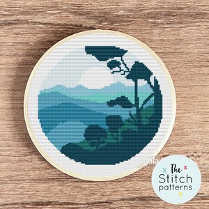 May include: A cross-stitch pattern featuring a blue and green landscape with a silhouette of trees in the foreground. The pattern is framed in a round wooden hoop.
