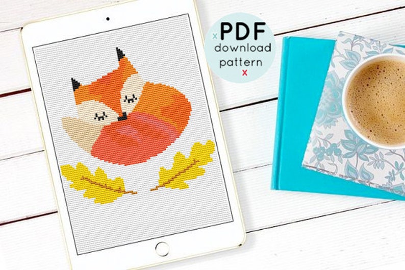 May include: A cross-stitch pattern featuring a sleeping fox with orange and white fur, curled up with its tail around its body. The pattern is surrounded by two yellow leaves.