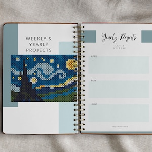 Pode incluir: Um caderno espiral com capa azul e branca. A p&aacute;gina da esquerda tem o texto "Weekly & Yearly Projects" e uma imagem de ponto cruz de uma noite estrelada. A p&aacute;gina da direita tem o texto "Yearly Projects Let's Stitch!" e uma lista de meses com espa&ccedil;os em branco para escrever.