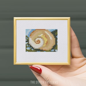 May include: A cross-stitch pattern of a seashell with a brown, yellow, and white color scheme. The seashell is surrounded by a blue and green background.