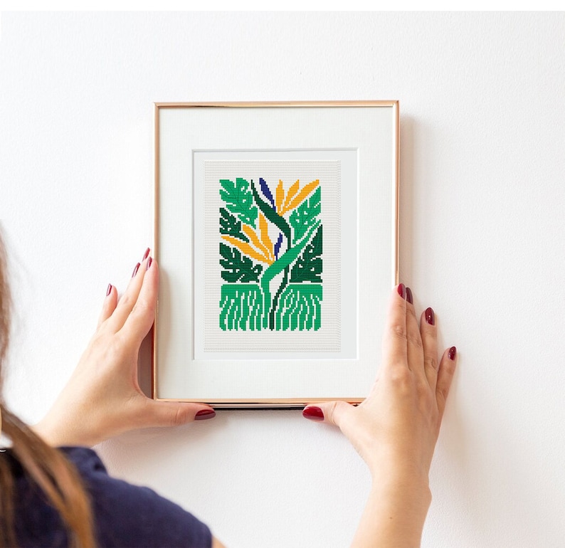 May include: A framed cross-stitch artwork featuring a stylized bird of paradise flower with green, yellow, and blue colors.