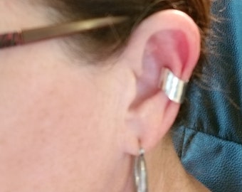 May include: A silver ear cuff worn on the upper part of the ear. The cuff is a simple, curved design.