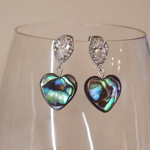 May include: A pair of silver earrings with a teardrop-shaped clear crystal and a heart-shaped iridescent abalone shell pendant.