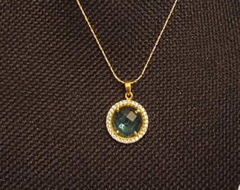 Colgante de topacio azul engastado con zafiros blancos y oro de 24 K sobre cadena de plata y baño de oro.