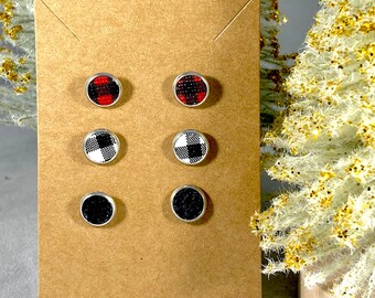 May include: A set of six stud earrings on a brown card. The earrings are round and have a silver backing. The earrings are in three different patterns: red and black plaid, black and white plaid, and solid black.