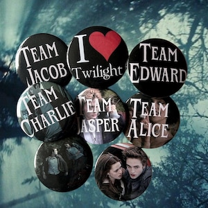 May include: A collection of black round buttons with white text and images. The buttons feature phrases like "Team Jacob," "Team Edward," and "Team Alice," along with images of characters and the text "I Twilight."