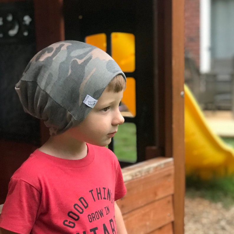 May include: A young child wearing a camouflage beanie and a red t-shirt with the text "Good Things Grow In Stars".