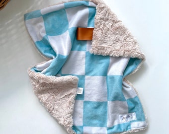 May include: A blue and white checkered baby blanket with a soft, plush beige border. The blanket has a brown leather tag with the text "Daily Miles" on it.
