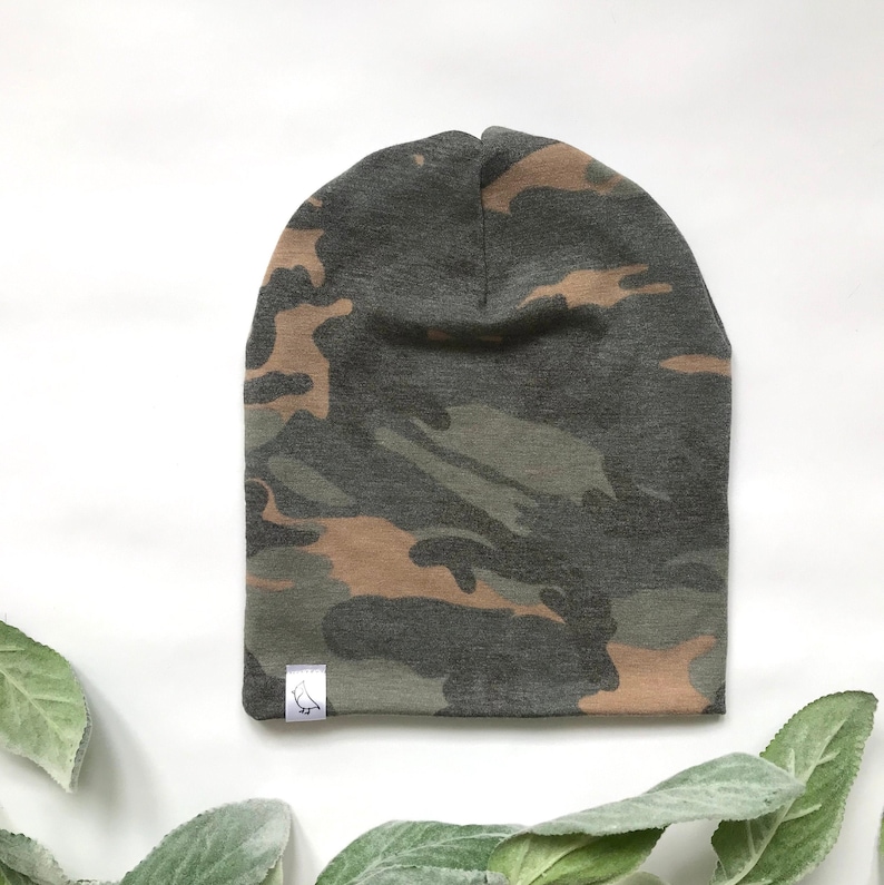 May include: A camouflage beanie hat with a brown, green, and gray pattern. The hat has a small white tag with a bird logo on the side.