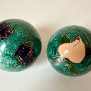 May include: Two decorative green spheres with floral and abstract designs. One sphere features a white flower with green leaves and a red accent. The other sphere has a dark blue and gold design.