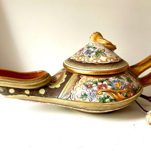 May include: A ceramic oil lamp with a lid, decorated with colorful floral patterns and gold accents. The lamp is in the shape of a genie lamp with a spout and a handle.