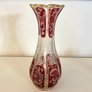 Puede incluir: Un jarrón de vidrio transparente con un diseño rojo y dorado. El jarrón tiene una boca ancha y un cuello estrecho. Está decorado con intrincados patrones florales.