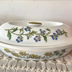 May include: White oval ceramic baking dish with a lid. The dish has a floral design with blue flowers and green leaves. The lid has a gold knob.