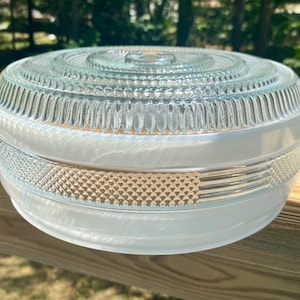 May include: A round glass light fixture cover featuring a clear top with concentric circular ridges and a textured diamond pattern band. The lower section is made of smooth, translucent white glass, creating a contrast between the clear and opaque elements.