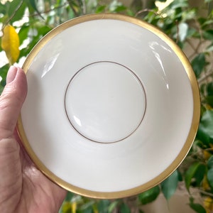 May include: White saucer with a gold rim. The saucer has a smaller, centered circle with a gold rim.