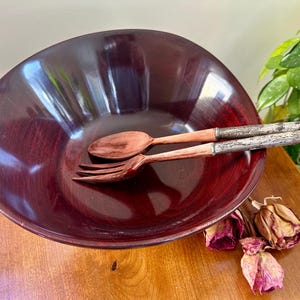 May include: A dark red wooden salad bowl with two wooden salad servers. The servers have silver handles.