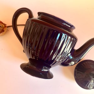 May include: A dark purple ceramic teapot with a ribbed design and a matching lid. The teapot has a classic shape with a rounded body and a spout on one side.