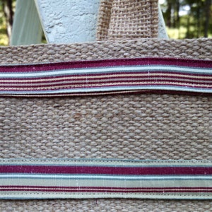 This shoulder bag will hold all you need each day. Muted stripes of deep red, wheat, sage from the purse&#39;s body accent the upper jute band.
