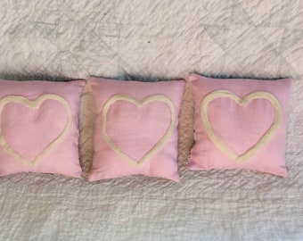 Mini decorative pillows feature an ivory wool needle felted heart on pink linen