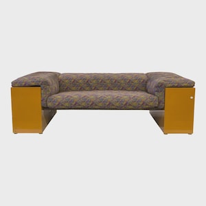 May include: A modern two-seater sofa with a geometric patterned fabric in shades of purple, green, and yellow. The sofa features mustard-yellow side panels and a low profile design, suitable for a living room or lounge area.