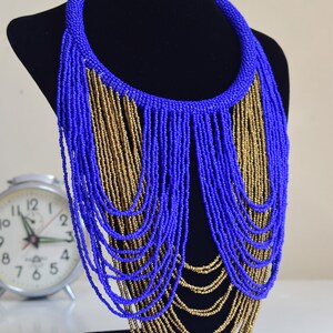 May include: A long, layered necklace made of blue and gold beads. The necklace is displayed on a black mannequin bust.