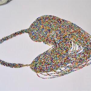 May include: A colorful beaded necklace with a long, cascading fringe. The necklace is made of small, multi-colored beads and has a gold clasp.