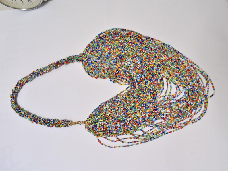 May include: A colorful beaded necklace with a long, cascading fringe. The necklace is made of small, multi-colored beads and has a gold clasp.